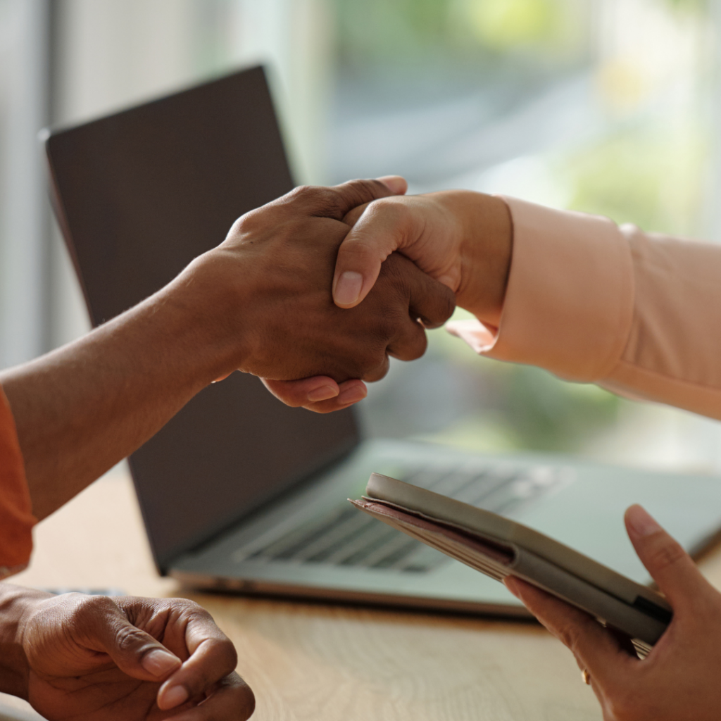 Shadow AI: How to Protect Your Business from Hidden AI Risks 1 HR and IT shaking hands with a laptop in the background, representing them working together to combat shadow AI.